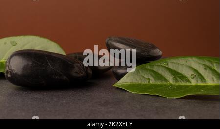 Massagesteine mit Blättern auf einem dunklen Steintisch Stockfoto