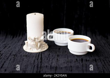 Kerze und zwei Tassen Kaffee auf schwarzem Hintergrund Stockfoto