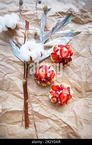 Schöne kleine Kuchen mit Erdbeeren zusammen mit einem Zweig auf Kraftpapier Stockfoto
