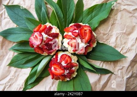 Schöne und helle kleine Kuchen mit Erdbeeren liegen auf grünen Blättern Stockfoto