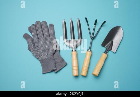 Gartengeräte zur Bearbeitungen im Garten und Textilhandschuhe auf blauem Hintergrund Stockfoto