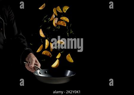 Zubereitungskoch bereitet Kartoffelkeile in der Pfanne zu Stockfoto