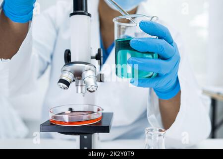 Asian Wissenschaftler Biochemiker oder Mikrobiologe arbeiten Forschung mit einem Mikroskop im Labor. Zum Schutz vor Ausbruch Coronavirus Covid19, Bakterien und Keimen. Stockfoto