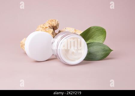 Offener Kosmetikbehälter mit weißer Creme, nahe dem Podium aus Naturstein und glänzenden Blättern, umweltfreundliches Konzept. Stockfoto