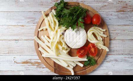 Camembert mit Streichkäse oder Käsepeitsche - salziger Snack-Käse mit Kirschtomaten und Kräutern auf Schneidebrett. Stockfoto