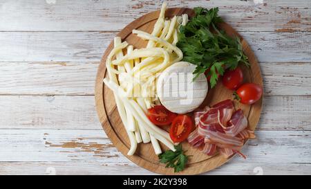 Auswahl an Käse und Scheiben geräuchertem Speck mit Kräutern und Kirschtomaten auf Holzschneidebrett Stockfoto