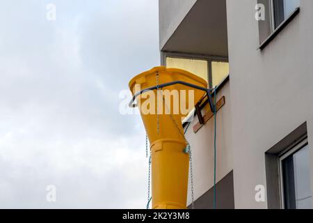 Die gelbe Schutsche oder die Rutsche an der Fassade des alten weißen Hauses hilft bei der Renovierung und Renovierung des alten Gebäudes für die saubere Beseitigung von Schutt und die Abfallentsorgung in den Container für die Baustelle Stockfoto