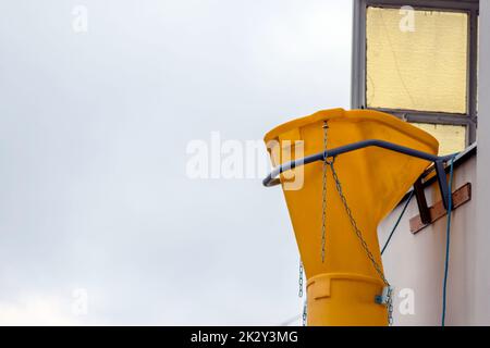 Die gelbe Schutsche oder die Rutsche an der Fassade des alten weißen Hauses hilft bei der Renovierung und Renovierung des alten Gebäudes für die saubere Beseitigung von Schutt und die Abfallentsorgung in den Container für die Baustelle Stockfoto