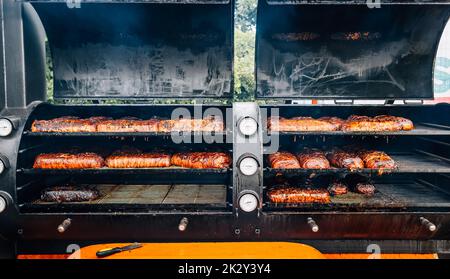 Großer Barbecue-Rauchergrill mit gegrilltem Fleisch und Speck Stockfoto