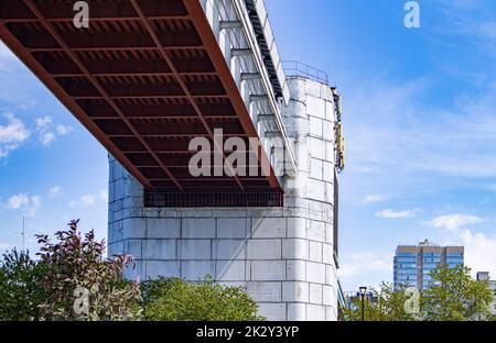 Technische Konstruktion der U-Bahn-Brücke mit Betonstützen, Ansicht von unten. Panorama der Stadt mit Himmel und Bäumen Stockfoto