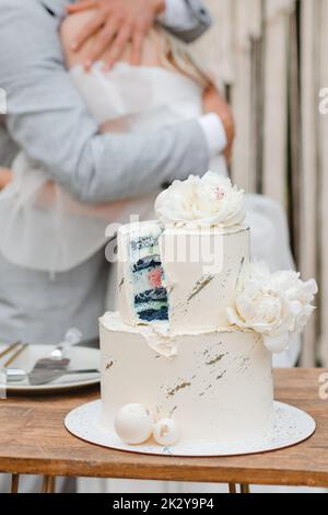 Eine geschnittene Hochzeitstorte mit blauer Torte und weißer Creme, und im Hintergrund umarmt der Bräutigam die Braut. Geschlechterparty-Konzept Stockfoto