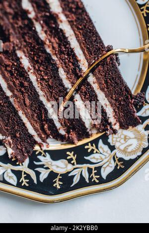 Devil's Food Schokoladenkuchen auf schwarzem, weiß floralem Goldteller mit Goldgabel Stockfoto