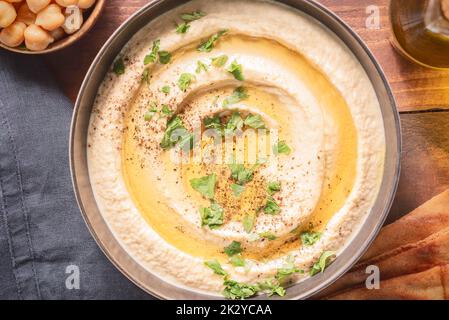 Arabische Küche; traditionelle cremige Hummus-Dip in dunkler Schüssel. Garniert mit Olivenöl, Paprika und Petersilie. Draufsicht mit Nahaufnahme. Stockfoto