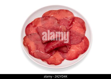 Auf weißem Schneideweg isolierte Scheiben in weißer Platte, italienische getrocknete Rindersalami aus Valtellina Stockfoto