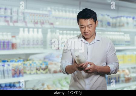 Asiatischer Käufer in einem Supermarkt in der Milchabteilung liest man Milch. Stockfoto