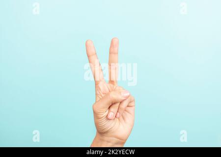 Handbewegung. Weibliche Hand zeigt die Nummer zwei. Hand zum Sieg, Friedenszeichen. Frau Hand zeigt nach oben mit den Fingern auf hellblauem Hintergrund Stockfoto