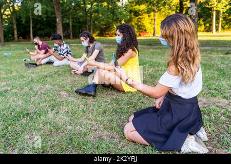 Eine Gruppe von multirassischen Freunden, die in einem öffentlichen Park im Freien sitzen und mit Smartphones Inhalte in sozialen Netzwerken teilen Stockfoto