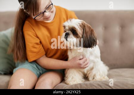 Porträt von niedlichen Mädchen mit Down-Syndrom spielen mit kleinen Hund, während auf der Couch zusammen sitzen, kopieren Raum Stockfoto