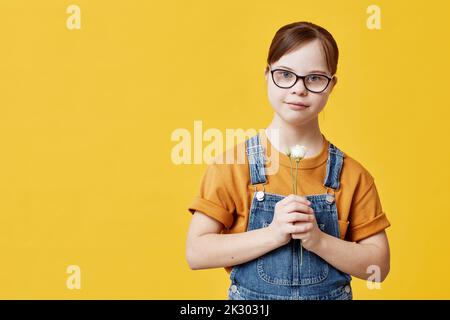 Waist-up-Porträt eines Teenagers mit Down-Syndrom, das im Studio vor gelbem Hintergrund die Kamera anschaut Stockfoto