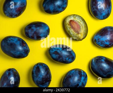 Pflaumen auf gelbem Hintergrund. Saftig geschnittene ​​plum. Stein in gelbem Fruchtfleisch. Gesundes Lebensmittelkonzept. Süße violette Sorte. Fruchtmuster. Eine Handvoll Obst Stockfoto