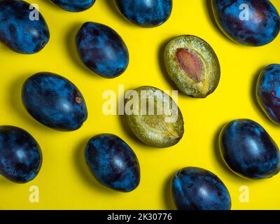 Pflaumen auf gelbem Hintergrund. Saftig geschnittene ​​plum. Stein in gelbem Fruchtfleisch. Gesundes Lebensmittelkonzept. Süße violette Sorte. Fruchtmuster. Eine Handvoll Obst Stockfoto