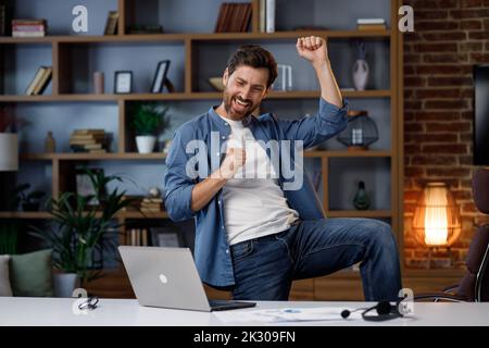 Ein gutaussehender männlicher Geschäftsmann beendete seinen Job erfolgreich und begann mit Vergnügen in seinem Heimbüro zu tanzen. Tanzender Manager Freiberufler am Ende Stockfoto