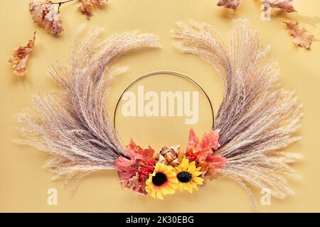 Hände, die getrockneten Blumenkranz aus trockenem Pampagras und Herbstblättern machen. Flach auf weiß gelbem Tisch, Sonnenlicht mit langen Schatten. Stockfoto