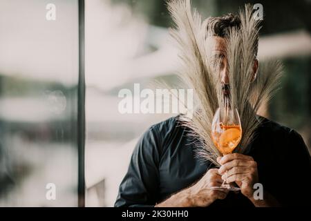 Mann mit Getränk, der das Gesicht mit Pampagras bedeckt Stockfoto