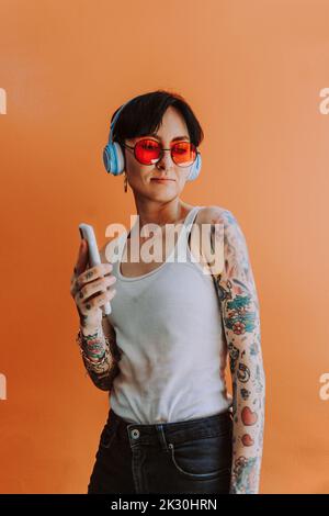 Schöne Frau, die über kabellose Kopfhörer vor orangefarbenem Hintergrund Musik hört Stockfoto