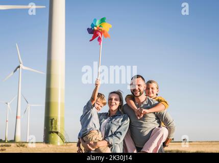 Optimistische Familie, die im Windpark steht, Sohn, der ein buntes Windrad trägt Stockfoto