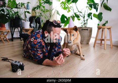 Lächelnder Mann mit Würstchen, der von einem Hund zu Hause liegt Stockfoto