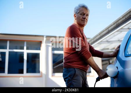 Ein älterer Mann lädt an einem sonnigen Tag ein Elektroauto Stockfoto