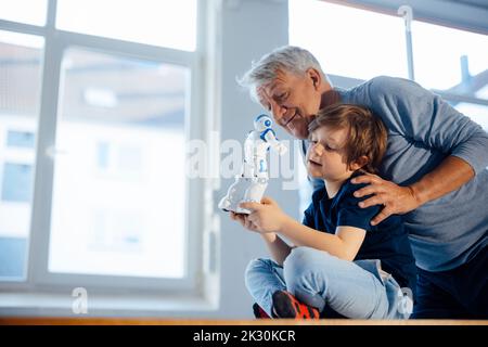 Lächelnder älterer Mann von Enkel mit Robotermodell zu Hause Stockfoto