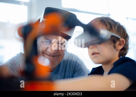 Lächelnder Großvater, der zu Hause vom Enkel ein Robotermodell ansieht Stockfoto