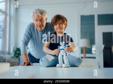 Lächelnder Junge, der zu Hause mit dem Robotermodell des Großvaters spielt Stockfoto