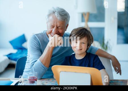 Glücklicher älterer Mann mit der Hand am Kinn von niedlichem Enkel zu Hause Stockfoto