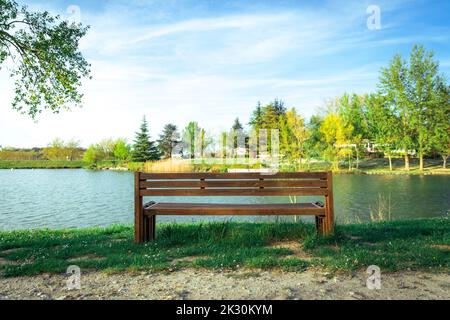 Leere Holzbank vor dem See im Park Stockfoto