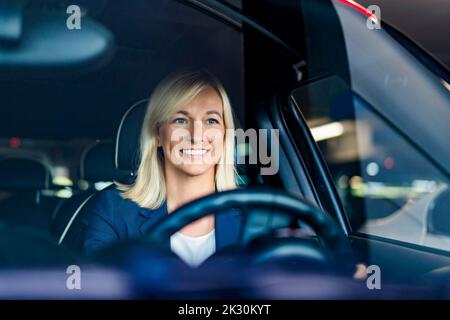 Glückliche Geschäftsfrau mit blonden Haaren Auto durch Windschutzscheibe gesehen fahren Stockfoto