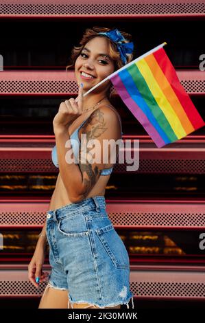 Lächelnde junge Frau mit Regenbogenfahne vor dem Verschluss Stockfoto