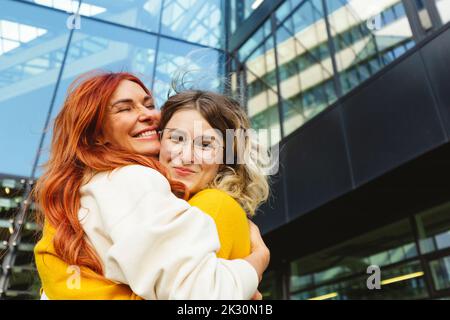 Glückliche Mutter umarmte Tochter vor dem Gebäude Stockfoto