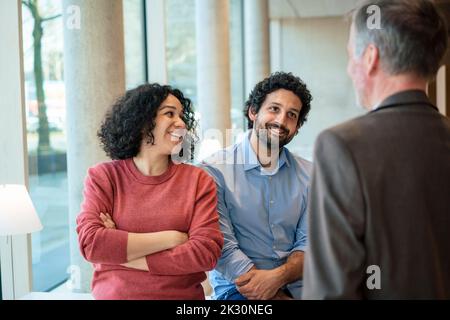 Glückliche, multirassische Kollegen diskutieren im Büro Stockfoto