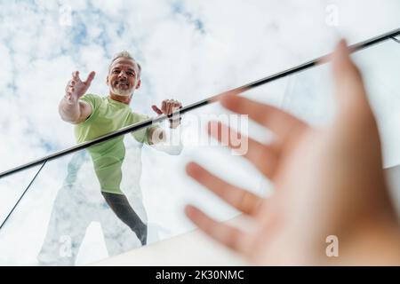 Lächelnder Mann, der nach der Hand eines Freundes greift Stockfoto