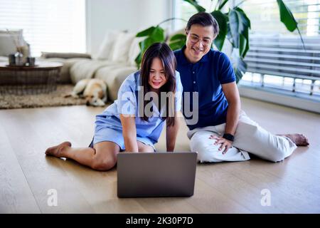Lächelnder Freiberufler mit Laptop von einem Mann im Wohnzimmer zu Hause Stockfoto
