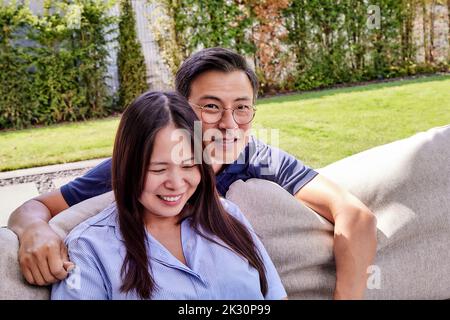 Lächelnder reifer Mann mit Brille von einer Frau, die auf dem Sofa sitzt Stockfoto