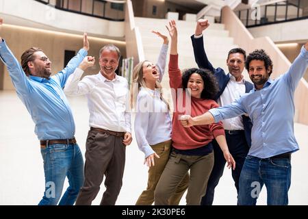 Fröhliche, multirassische Geschäftskollegen, die in der Lobby Erfolge feiern Stockfoto