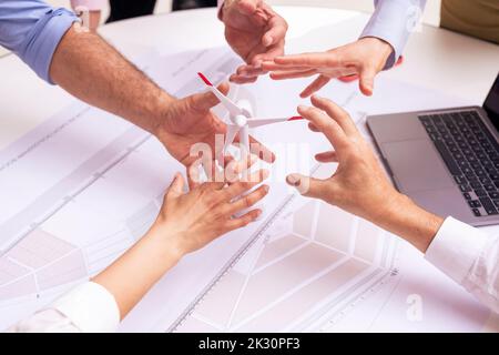 Hände von Geschäftskollegen mit Windenergieanlagenmodell auf dem Tisch Stockfoto