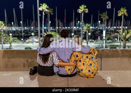 Junge Freunde sitzen nachts mit Armen um sich herum Stockfoto