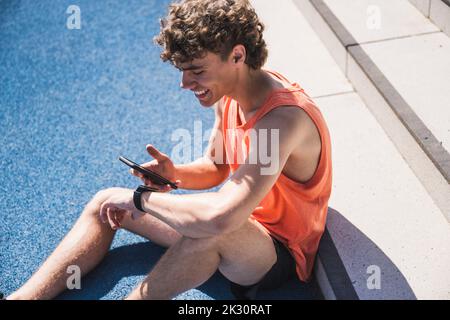 Glücklicher Sportler mit Smartphone vor der Treppe sitzen Stockfoto