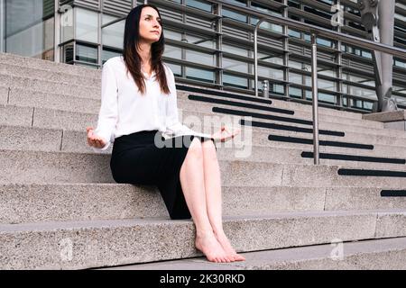 Kontemplative Frau, die auf der Treppe sitzt und vor dem Bürogebäude meditiert Stockfoto