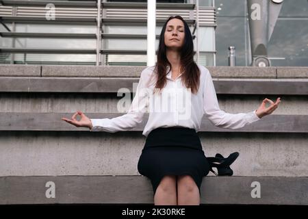 Reife Geschäftsfrau meditiert auf Stufen vor dem Bürogebäude Stockfoto